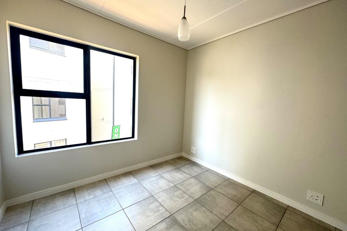 A bright, empty bedroom featuring neutral wall paint, large black aluminium-framed windows, and modern tiled flooring.