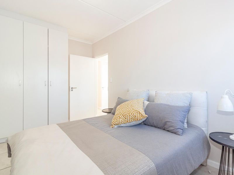 A bright and well-maintained bedroom featuring neutral walls, tiled flooring, and ample built-in cupboard storage.