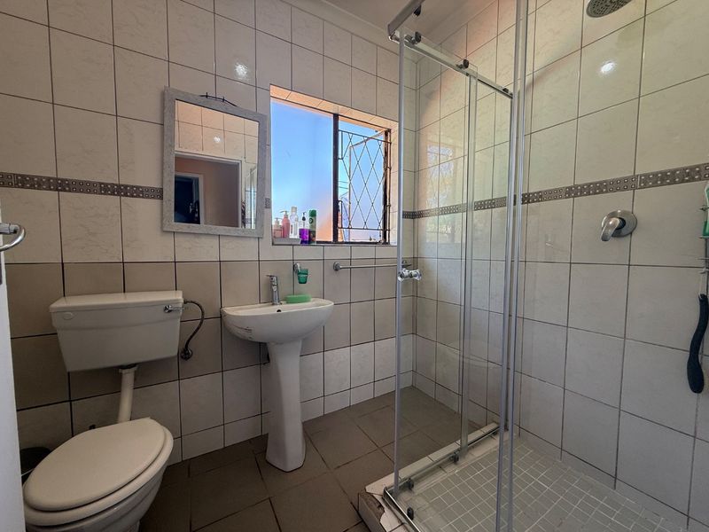 A functional bathroom featuring a pedestal basin, toilet, and a glass-enclosed shower with tiled finishes throughout.