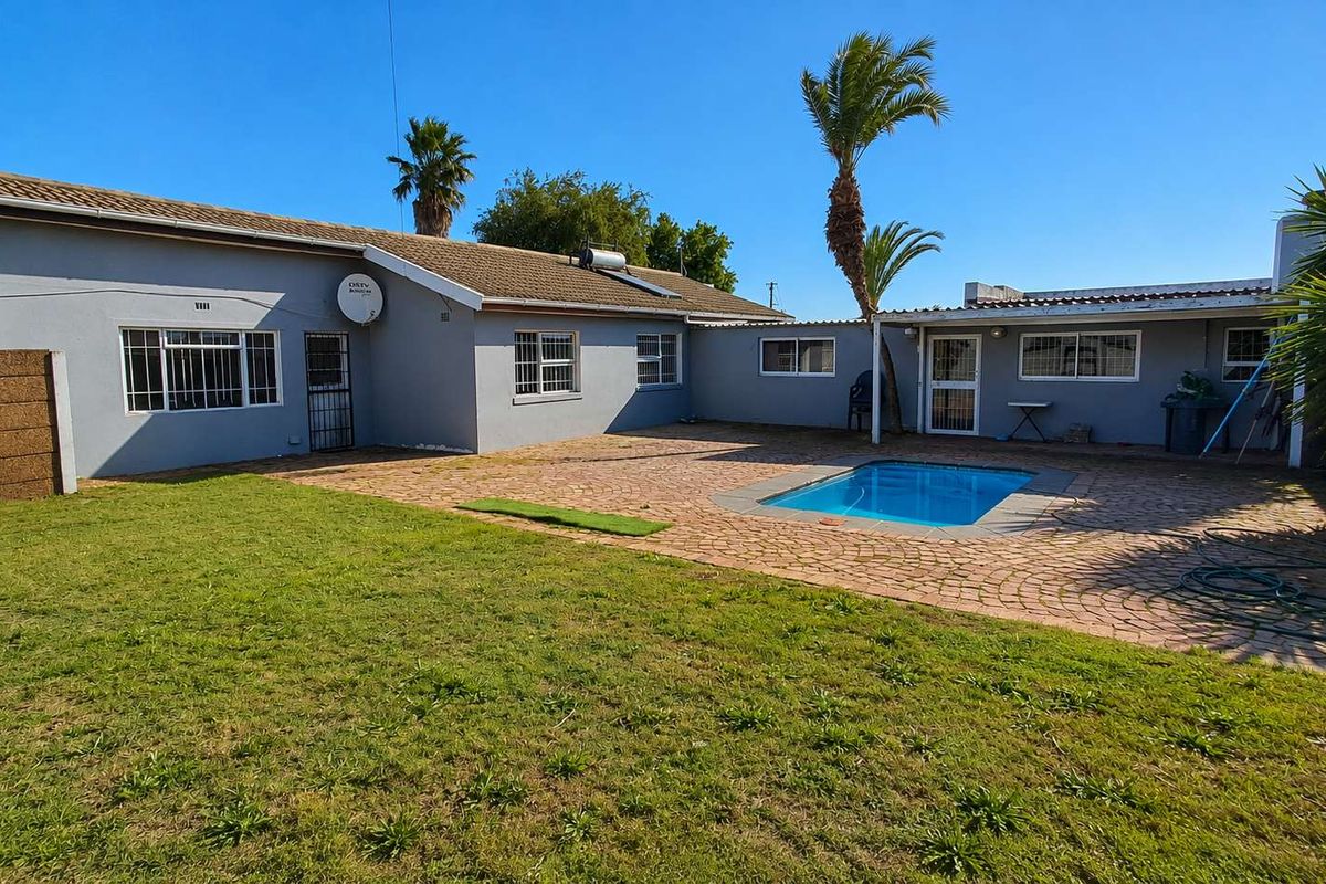 Rear exterior view featuring a swimming pool, paved patio area, and a spacious garden with established palm trees.