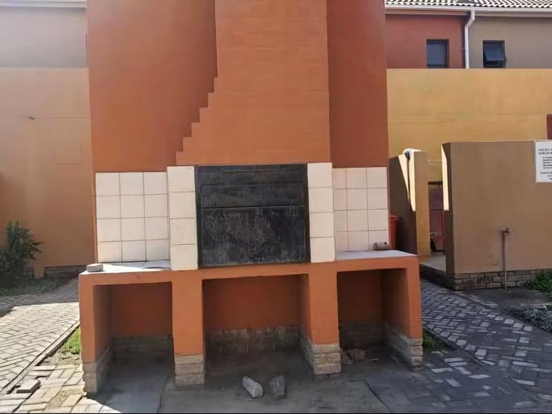 An outdoor area featuring a built-in brick braai structure set within a paved courtyard, showing signs of wear and maintenance requirements.