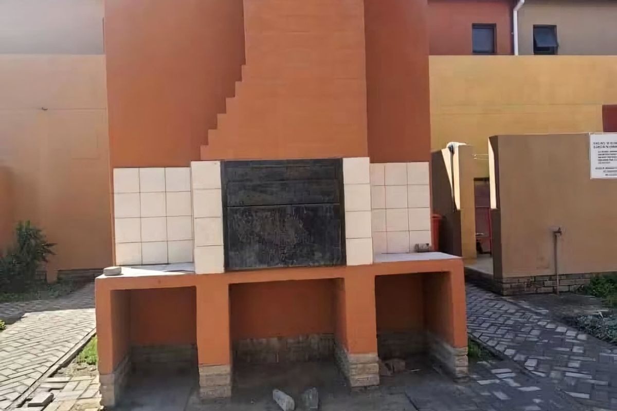 An outdoor area featuring a built-in brick braai structure set within a paved courtyard, showing signs of wear and maintenance requirements.