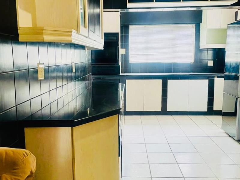 A spacious kitchen featuring high-contrast black and white cabinetry, tiled backsplash, and tiled flooring with ample counter space.