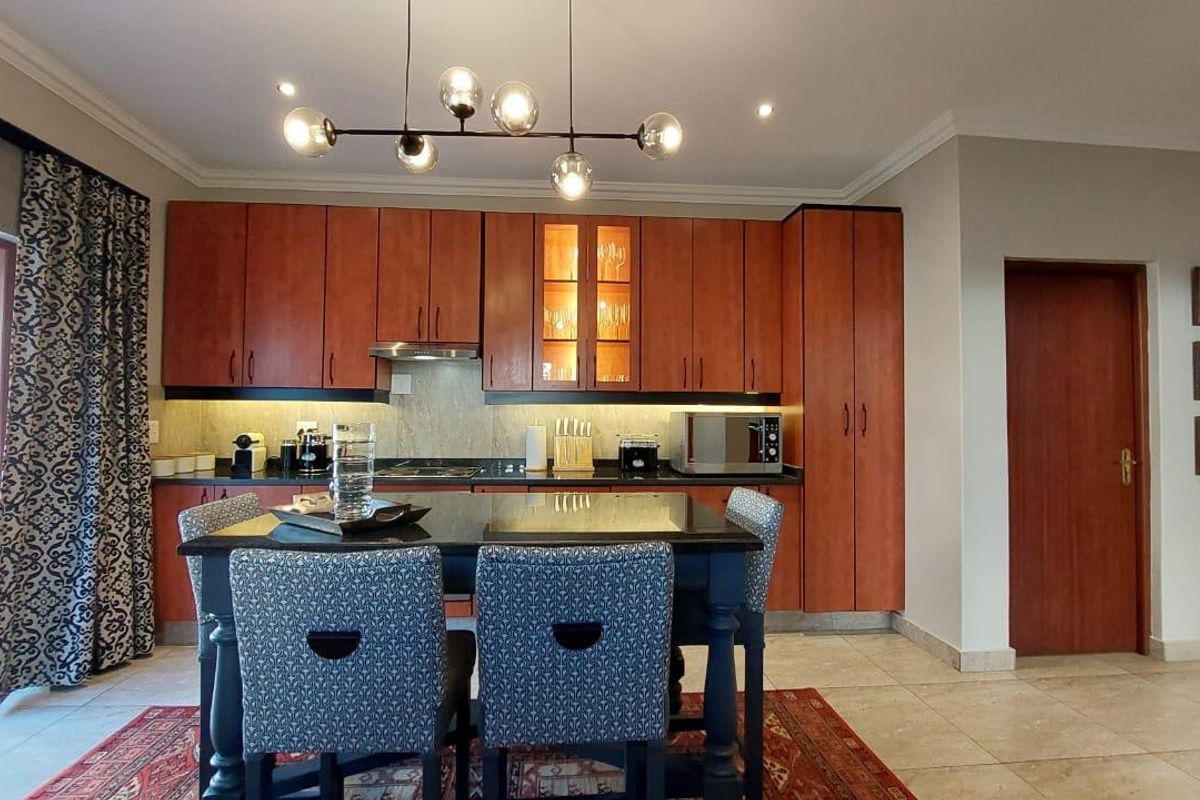 A well-maintained kitchen featuring warm-toned wooden cabinetry, granite countertops, integrated hob, and extractor fan, with direct access to an outdoor patio area.