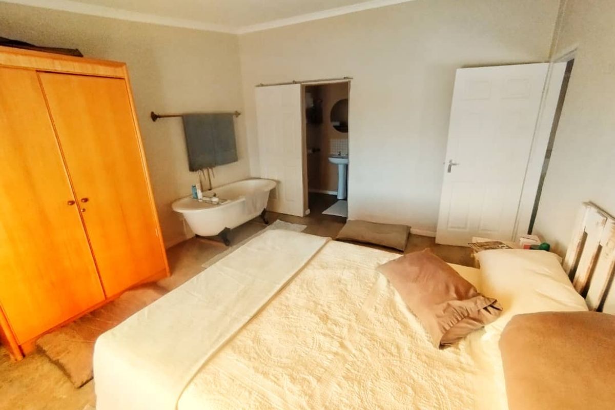A bedroom featuring a unique integrated clawfoot bathtub, neutral walls, and access to an adjoining bathroom area.