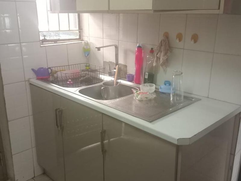 A compact scullery or utility area featuring built-in cabinetry, a stainless steel sink with mixer tap, and tiled splashback finishes.