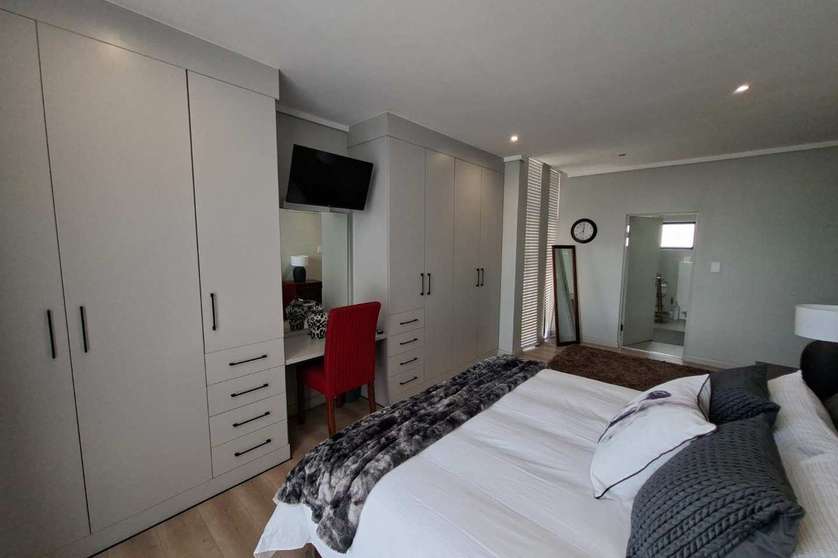 Spacious bedroom featuring extensive built-in cabinetry with an integrated vanity, recessed lighting, and modern laminate flooring.
