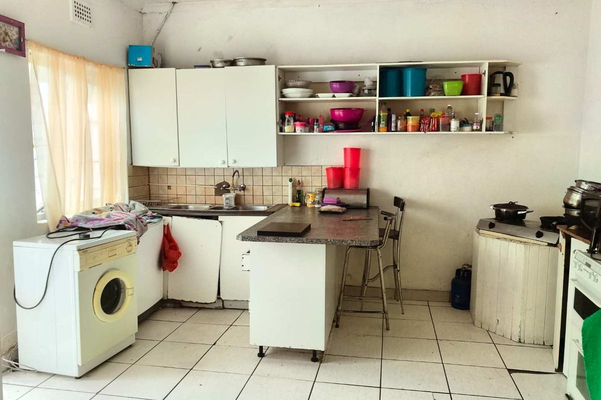 A dated kitchen featuring white cabinetry, tiled flooring, a breakfast bar, and integrated sink area, requiring cosmetic updates and maintenance.