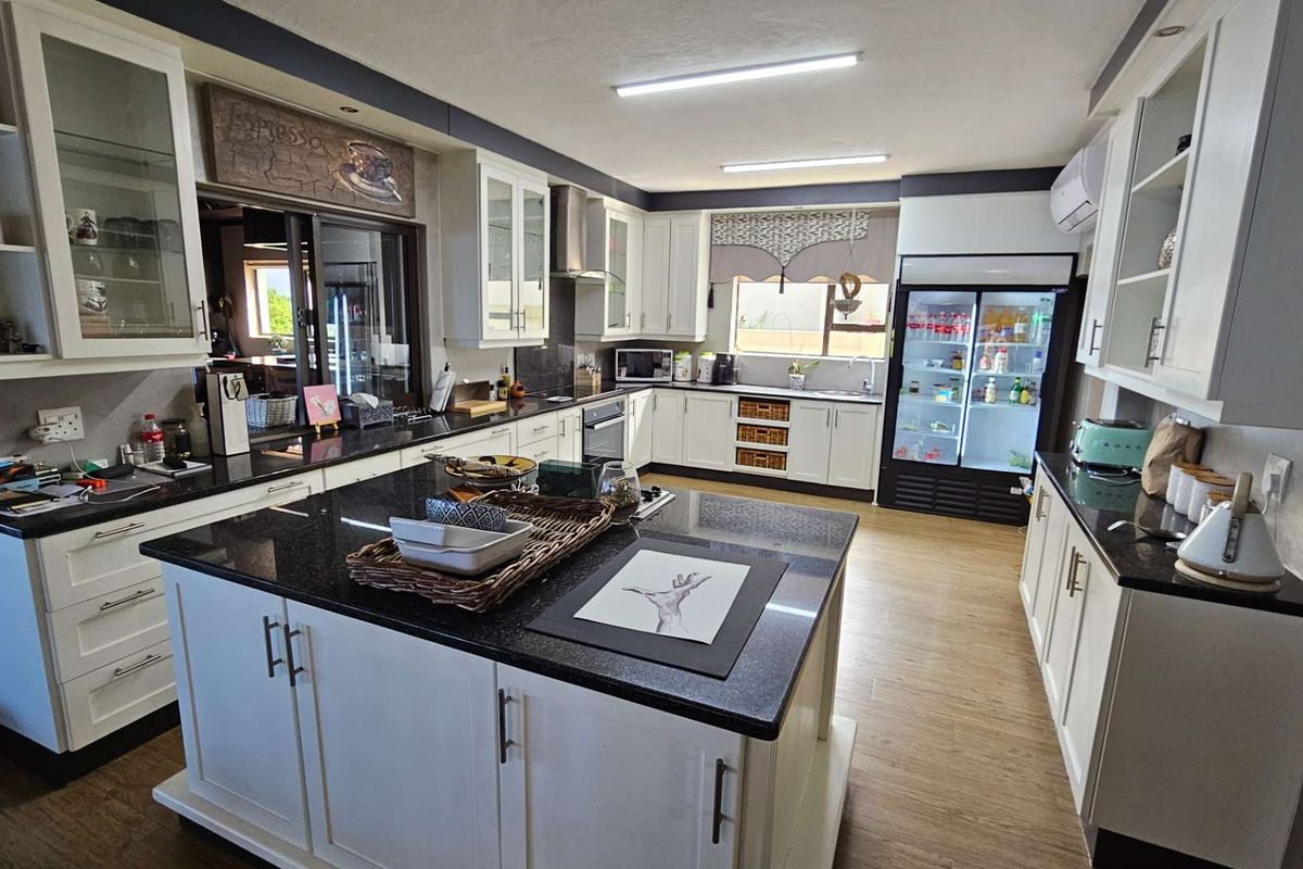 Spacious kitchen featuring a large central island, granite countertops, ample white cabinetry, and integrated appliances, providing a functional and well-lit culinary workspace.