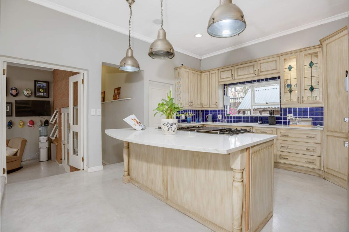 A kitchen featuring a central island with a stone countertop, built-in cabinetry, a gas hob, and a blue tiled backsplash.