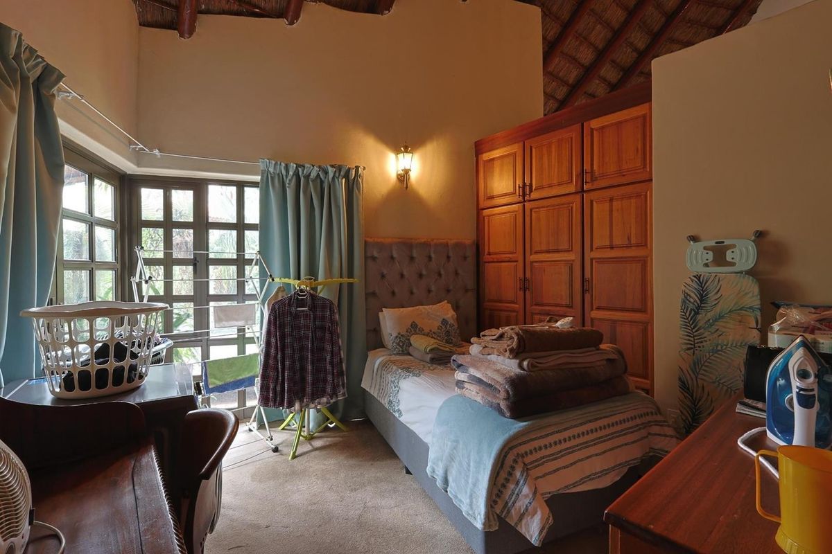 A bedroom featuring a high thatched ceiling, built-in wooden cupboards, and large windows allowing natural light.