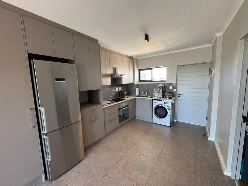 Modern kitchen featuring neutral-toned cabinetry, tiled flooring, integrated appliances, and a functional layout with a dedicated laundry area.