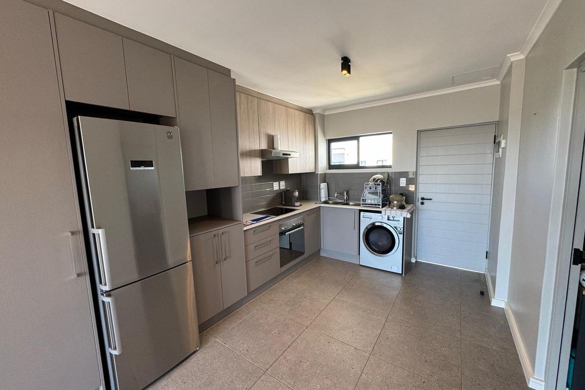 Modern kitchen featuring neutral-toned cabinetry, tiled flooring, integrated appliances, and a functional layout with a dedicated laundry area.