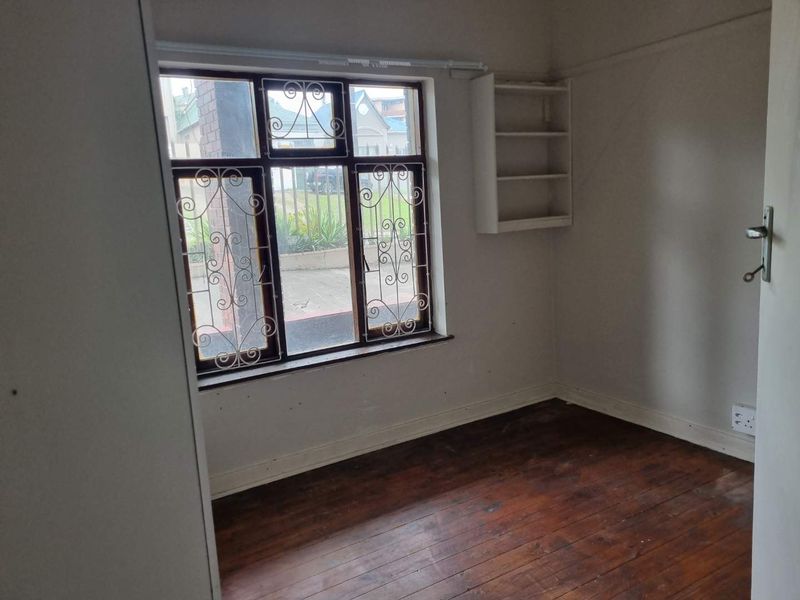 An empty bedroom featuring original timber flooring, built-in wall shelving, and a window fitted with security bars.