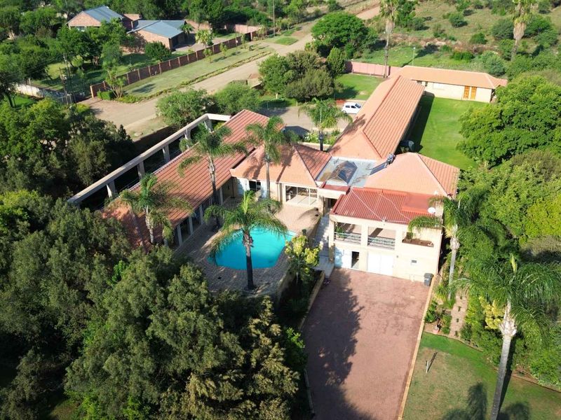 Aerial view of a large residential property featuring a swimming pool, extensive garden, paved driveway, and multiple roof sections.