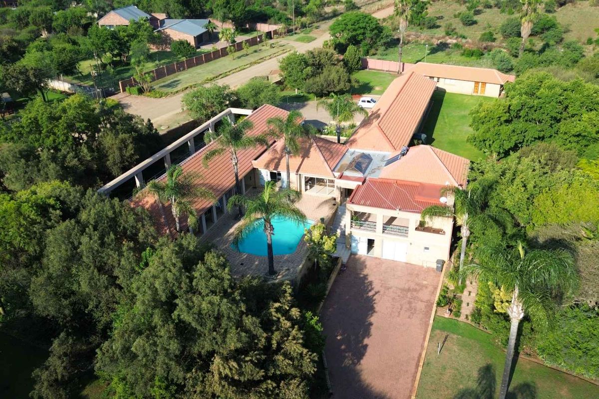 Aerial view of a large residential property featuring a swimming pool, extensive garden, paved driveway, and multiple roof sections.