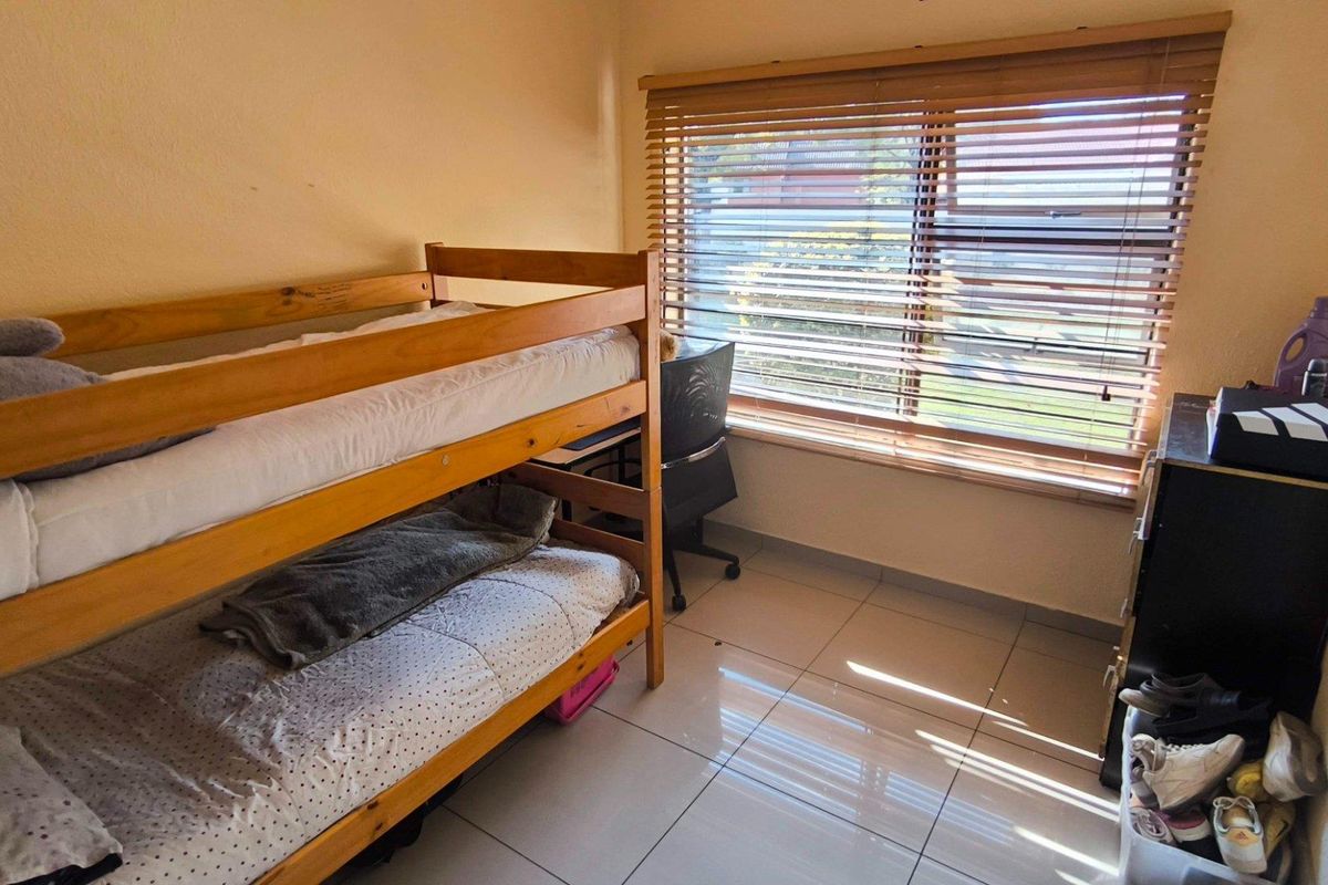 A functional bedroom featuring tiled flooring and wooden venetian blinds, providing a bright and practical living space.