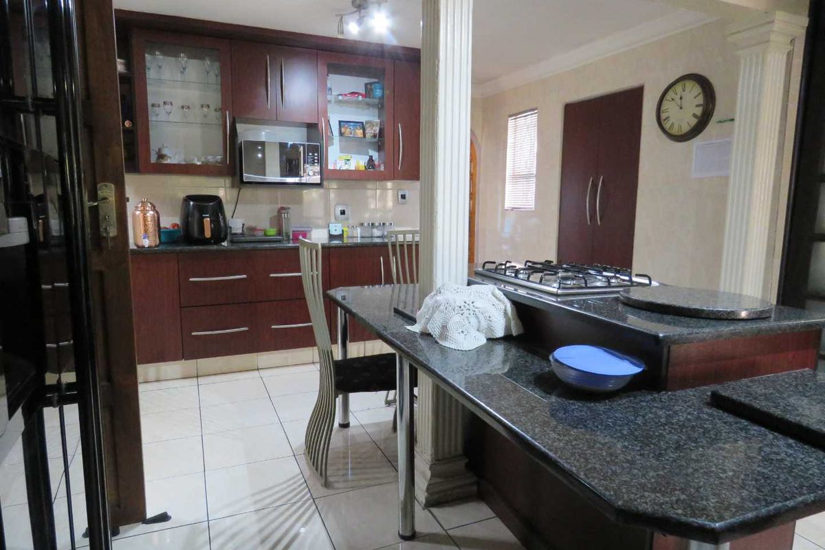 A functional kitchen featuring dark wood cabinetry, granite countertops, a built-in gas hob, and tiled flooring with a breakfast bar island.