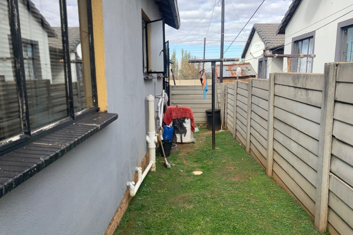A narrow side exterior area of the townhouse featuring a concrete boundary wall, exposed plumbing, and a small grass patch.