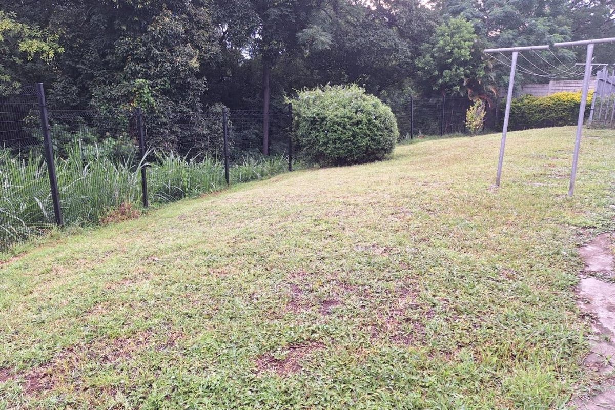 A spacious backyard area featuring a grass lawn, perimeter wire mesh fencing, and a fixed metal washing line.