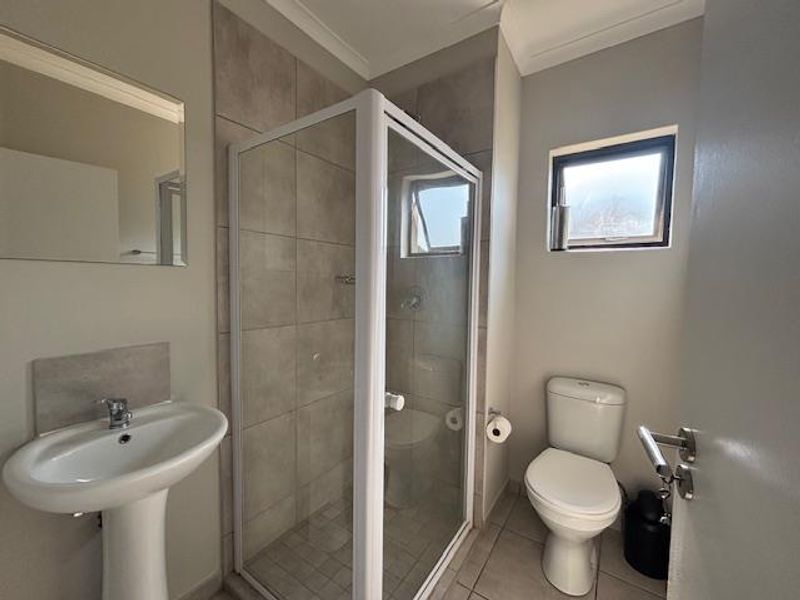 A clean and functional bathroom featuring a pedestal basin, a glass-enclosed shower with tiled walls, and a standard toilet.