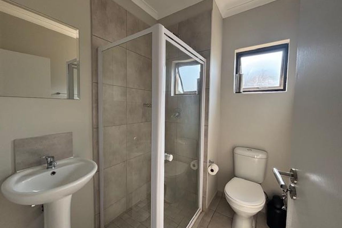 A clean and functional bathroom featuring a pedestal basin, a glass-enclosed shower with tiled walls, and a standard toilet.