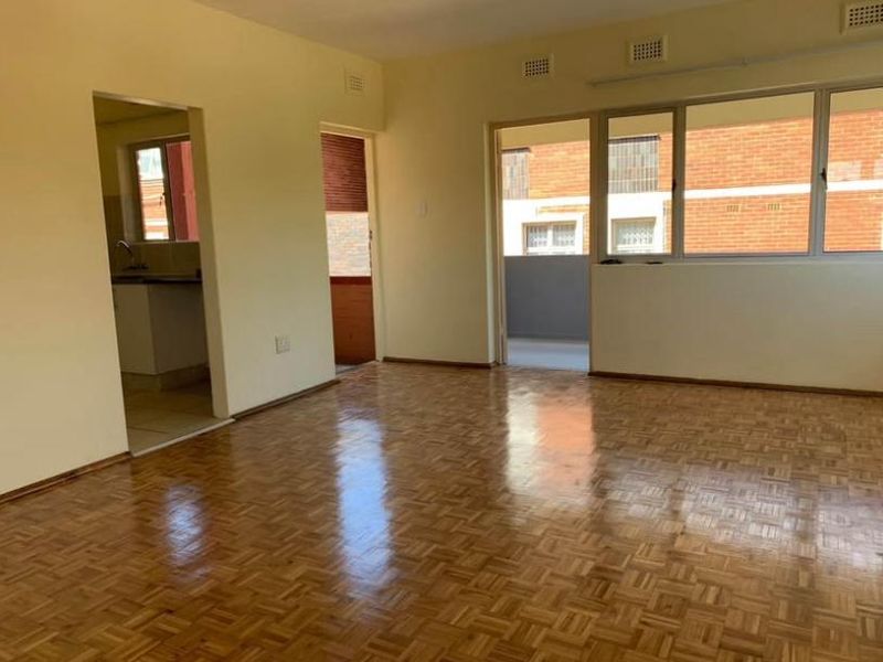 Spacious living area featuring polished parquet flooring, large windows, and direct access to an outdoor balcony, offering a bright and versatile living space.