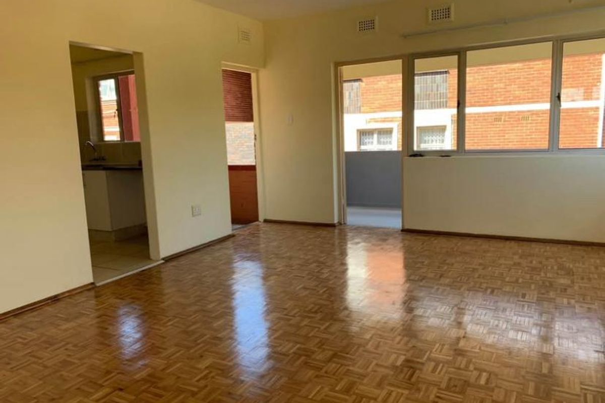 Spacious living area featuring polished parquet flooring, large windows, and direct access to an outdoor balcony, offering a bright and versatile living space.