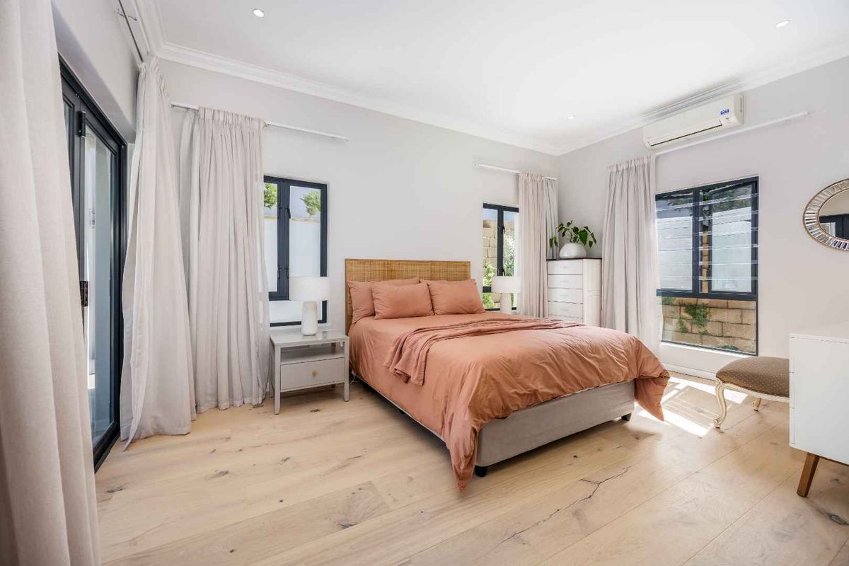 A bright and modern bedroom featuring light wood flooring, recessed lighting, a split-system air conditioner, and direct access to an outdoor area via sliding doors.