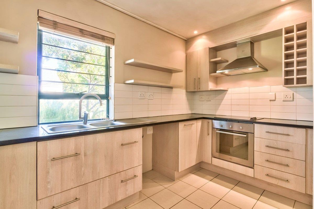 A clean and functional kitchen featuring light wood-tone cabinetry, dark countertops, built-in oven, extractor fan, and a convenient wine rack.