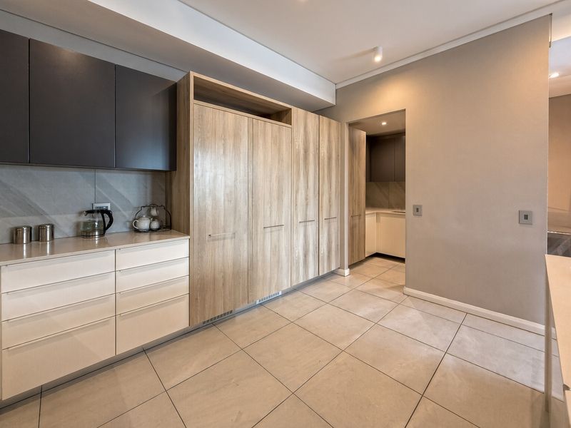 A modern, well-appointed scullery featuring sleek built-in cabinetry, stone countertops, and neutral tiled flooring, providing ample storage and prep space.