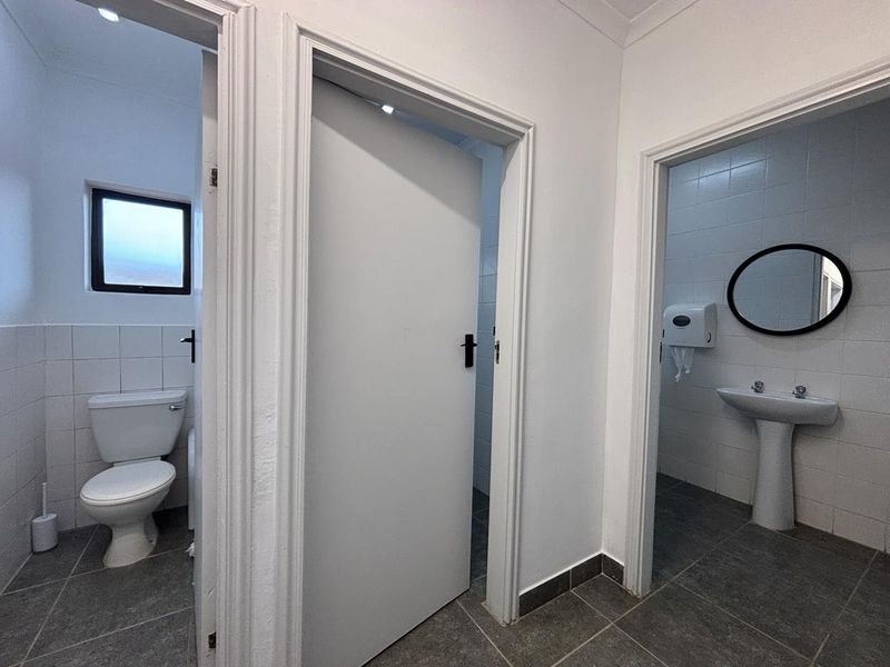 A clean hallway providing access to two separate restroom facilities, featuring tiled flooring and functional sanitary fixtures.