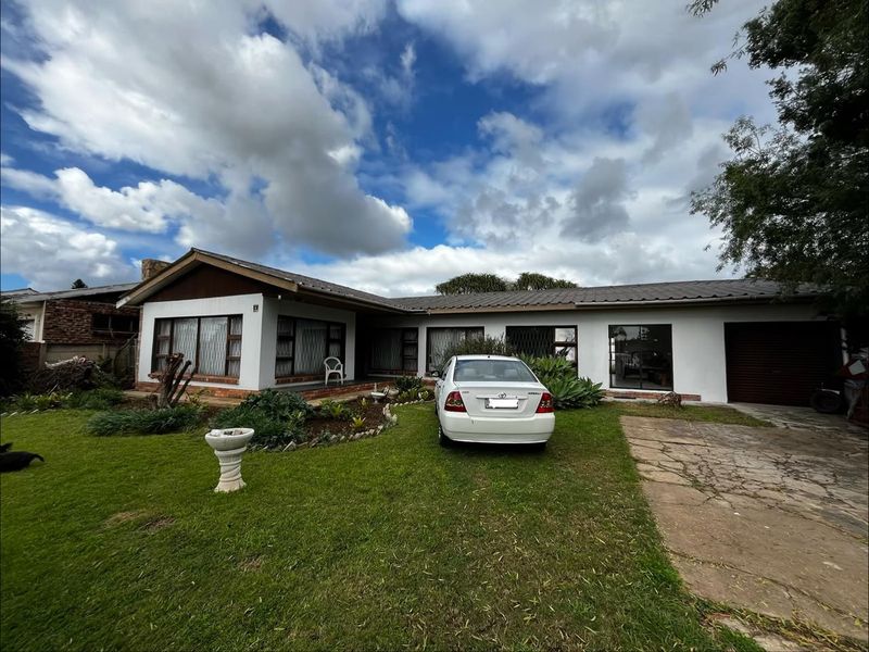 Front elevation of a cottage-style home featuring a metal roof, brick and plaster facade, paved driveway, and established garden.
