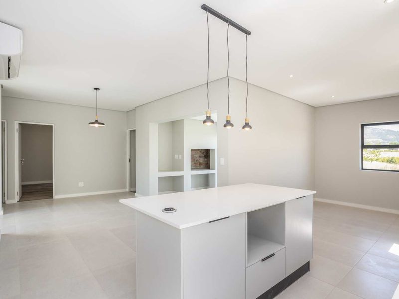 Modern open-plan living area featuring a central kitchen island, sleek tiled flooring, contemporary pendant lighting, and a split-system air conditioner.