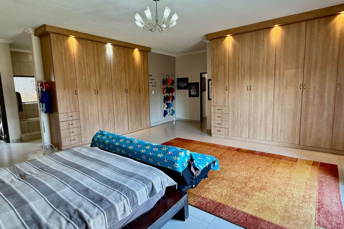 Spacious bedroom featuring extensive built-in wooden cabinetry with integrated downlighting and tiled flooring.