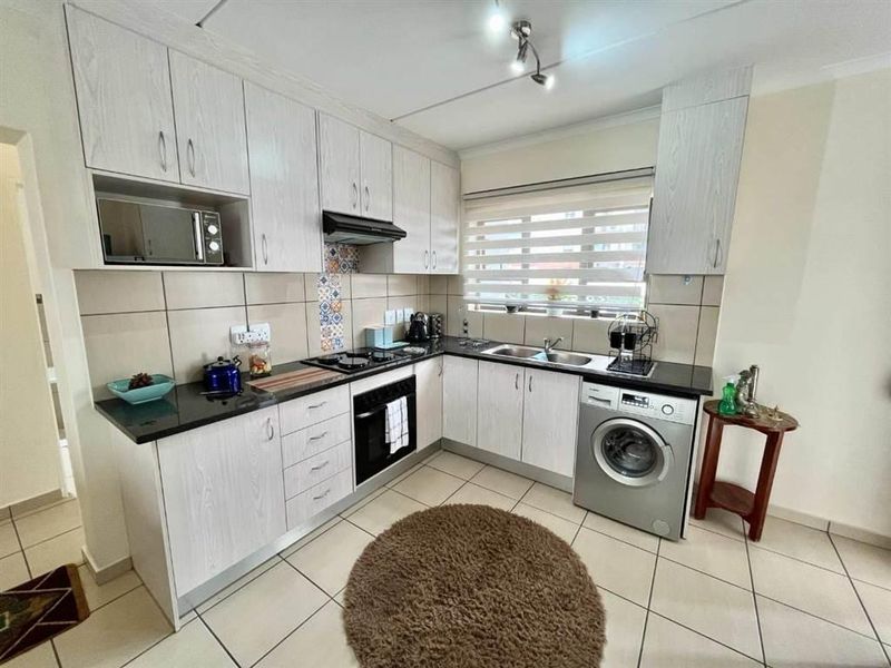 A functional kitchen featuring light wood-grain cabinetry, granite countertops, a built-in oven with hob, and integrated laundry appliance space.