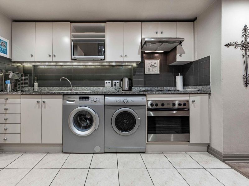A functional laundry area featuring built-in cabinetry, granite countertops, a stainless steel sink, integrated oven, extractor fan, and tiled finishes.