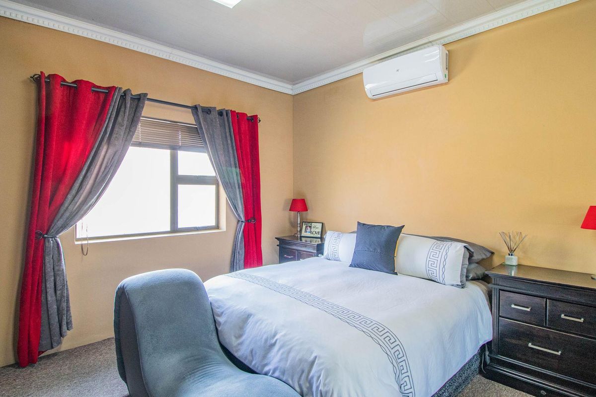 A well-maintained bedroom featuring a wall-mounted air conditioning unit, built-in cupboards, and neutral wall finishes.