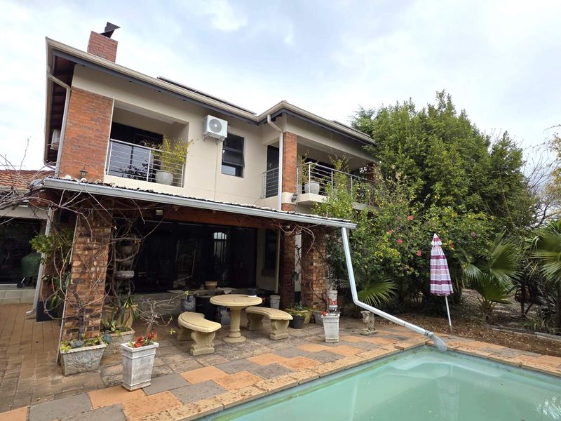 Rear view of a two-story house featuring a covered patio, upper-level balconies with stainless steel railings, and a swimming pool set in a garden.