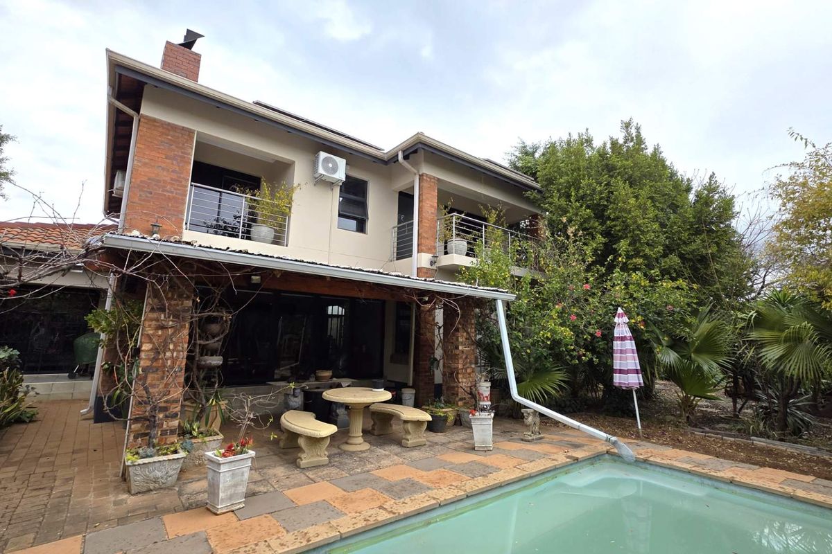 Rear view of a two-story house featuring a covered patio, upper-level balconies with stainless steel railings, and a swimming pool set in a garden.