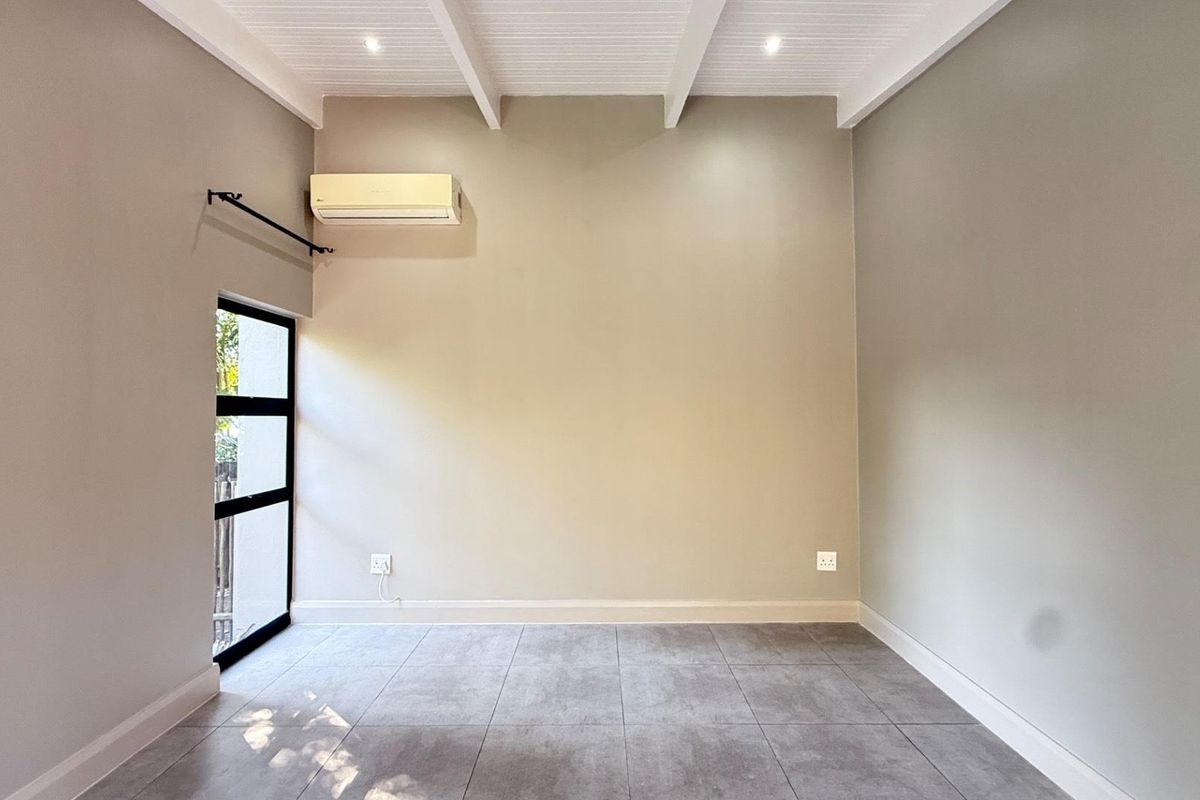 A bright, empty living space featuring tiled flooring, exposed beam ceiling, and a wall-mounted air conditioning unit.
