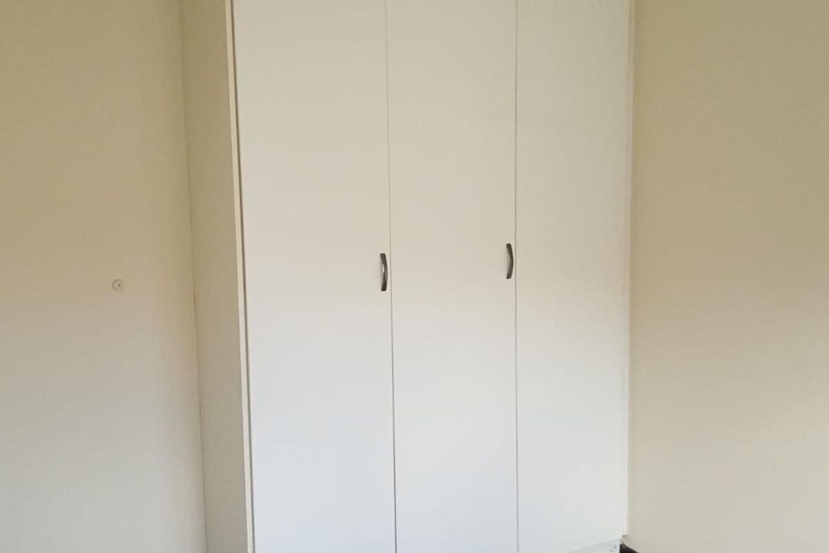 A bedroom featuring a built-in white wardrobe with three doors and neutral carpeting.