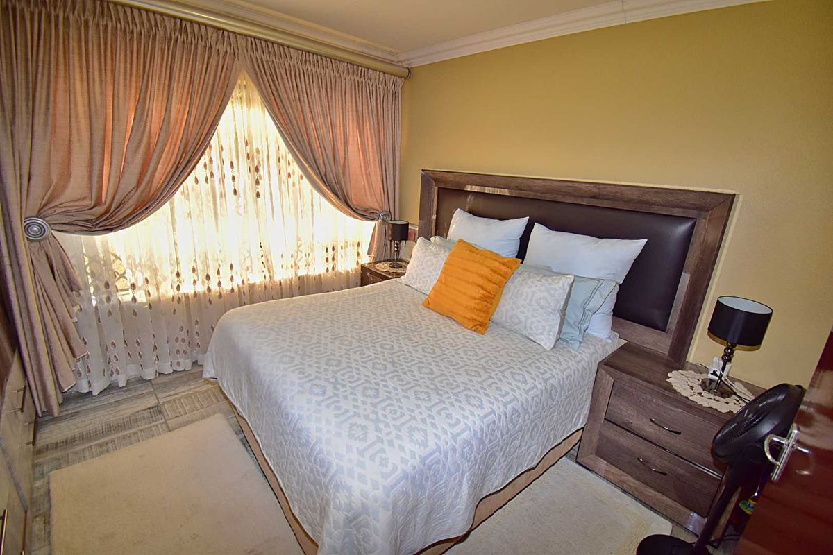 A well-lit bedroom featuring neutral wall tones, crown molding, and a large window with layered drapery.
