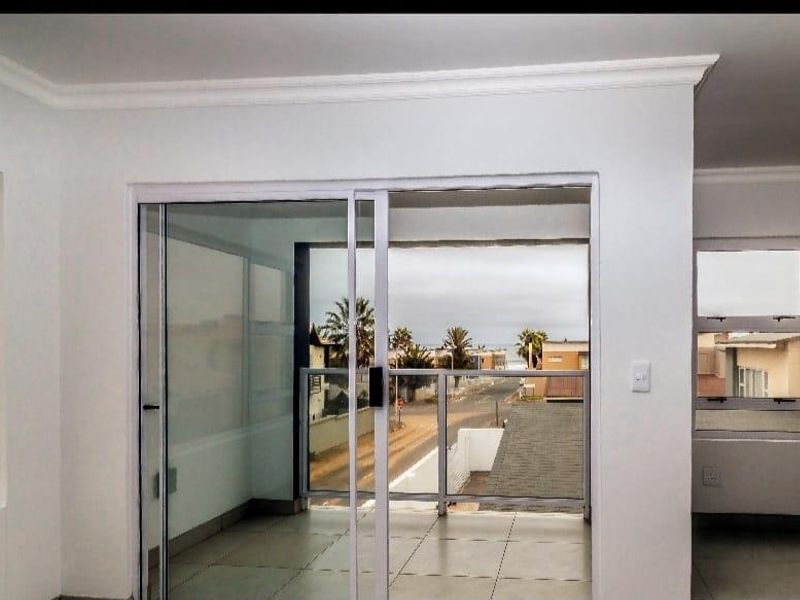 Bright living area featuring large sliding glass doors that open onto a tiled balcony with a glass balustrade and neighbourhood views.