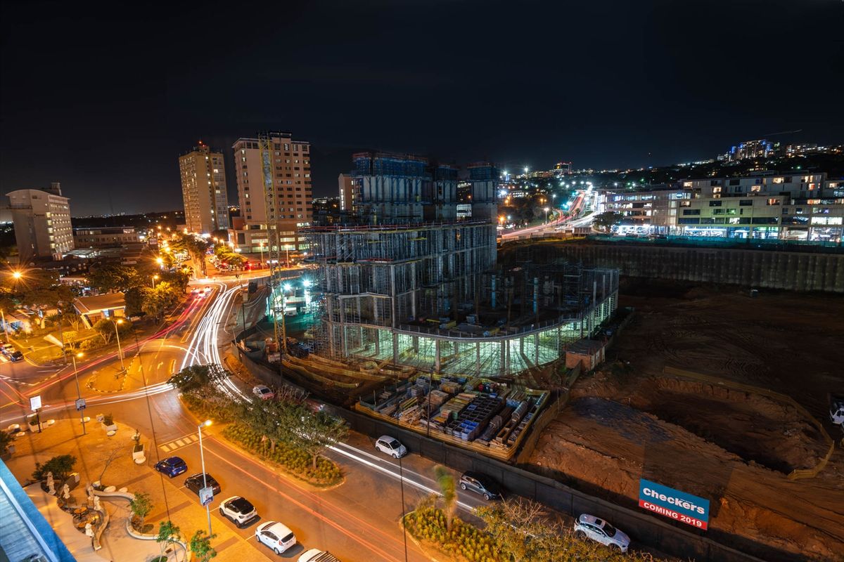 An elevated night view of an active urban construction site featuring surrounding city infrastructure and road networks.