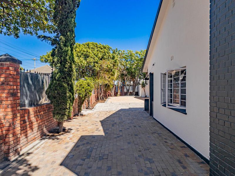A well-maintained rear exterior area featuring neat brick paving, a secure face brick boundary wall with electric fencing, and a clean painted facade.