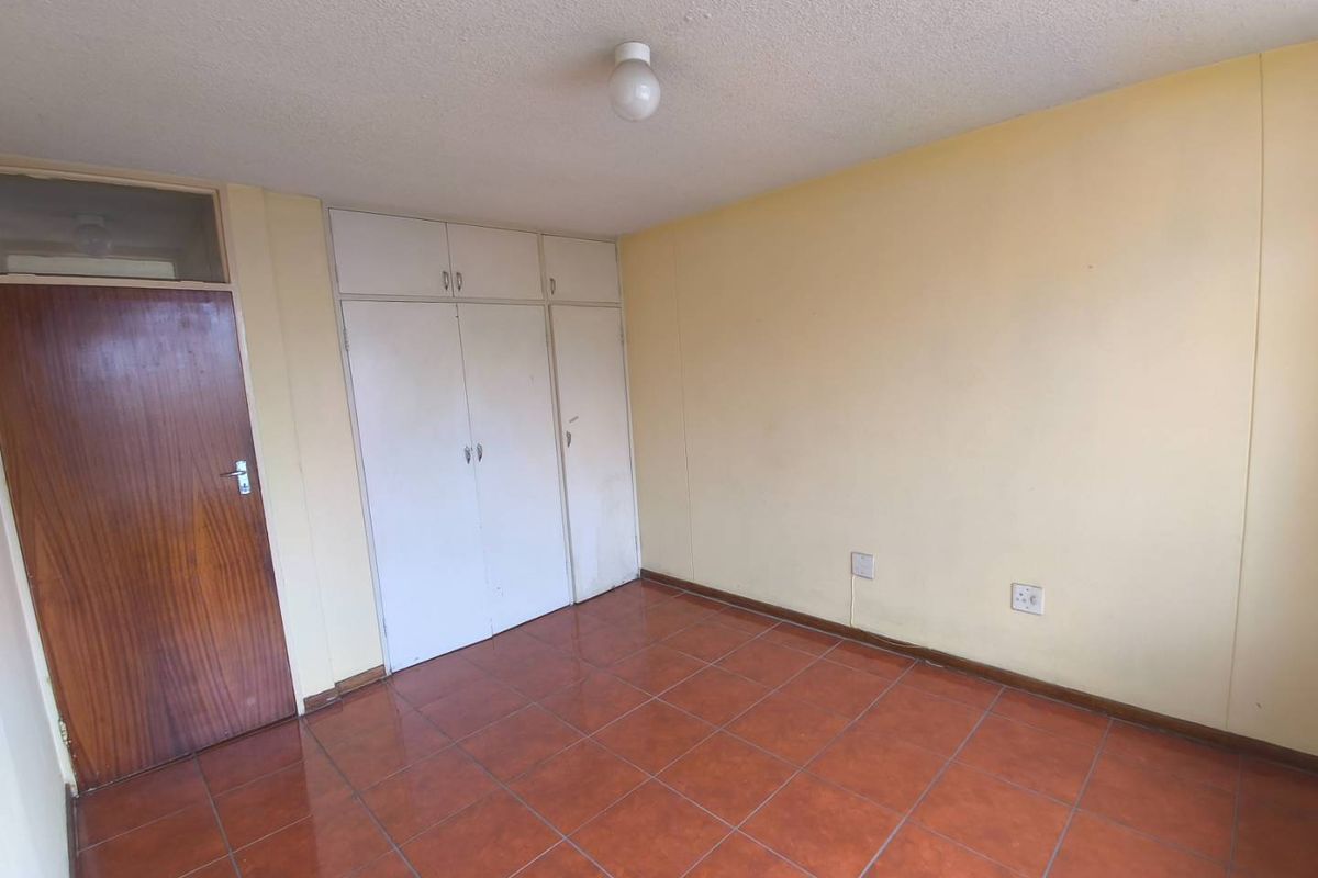 A vacant bedroom featuring tiled flooring, built-in storage cupboards, and a standard wooden door.