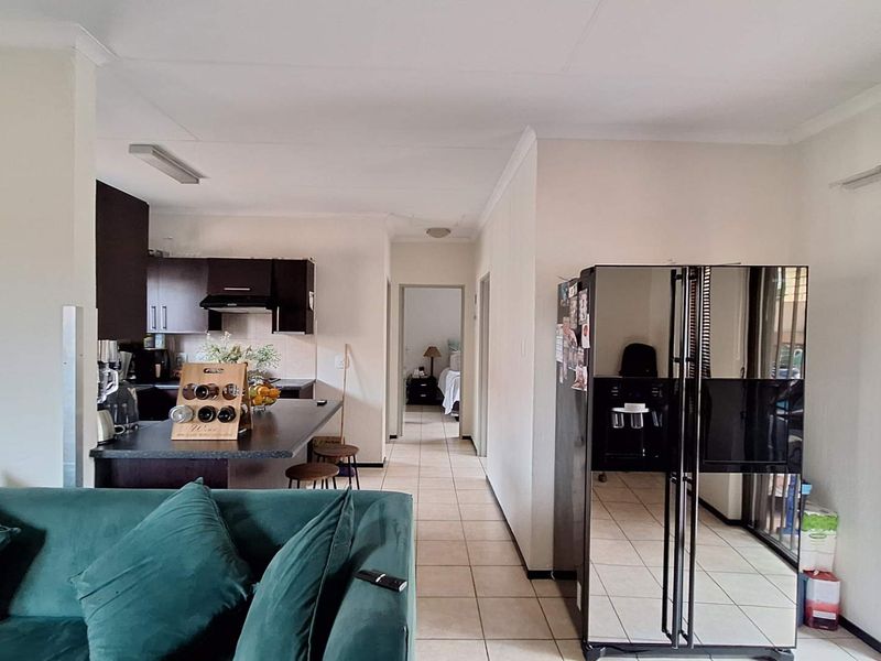 Open-plan living area featuring a kitchen with dark cabinetry, a breakfast island, and tiled flooring throughout, leading to a hallway and adjacent living space.