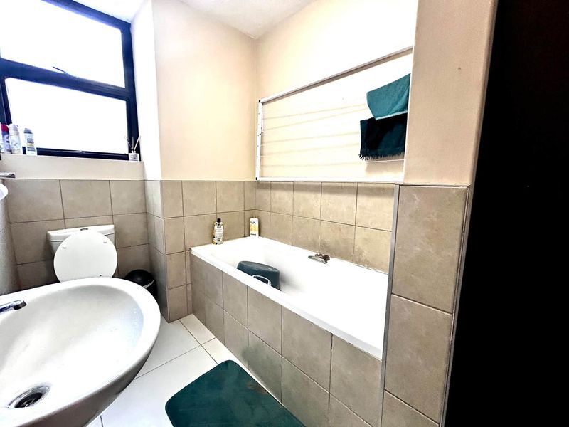 A functional bathroom featuring a bathtub, pedestal basin, and toilet with neutral wall tiling and a wall-mounted drying rack.