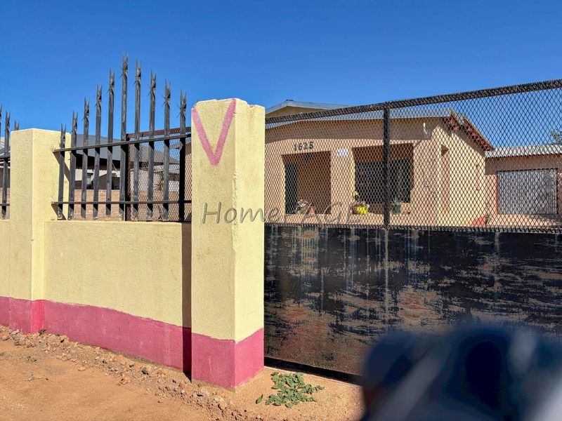 Front view of the property featuring a perimeter wall with metal security fencing and a sliding gate.
